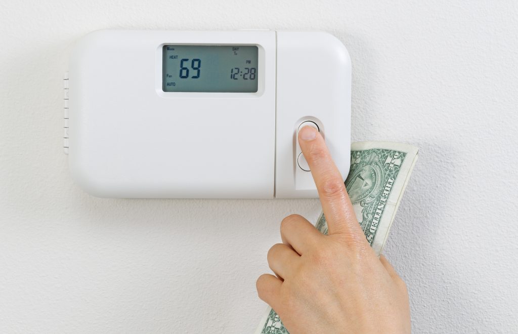 Gros plan d'un main tenant un billet qui règle un thermostat.