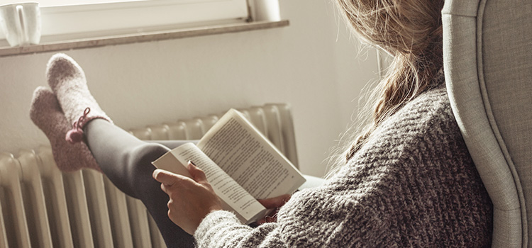 jeune femme lisant un livre devant un radiateur